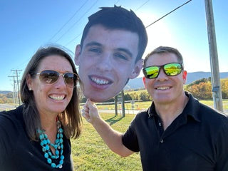 Parents holding a custom giant photo head cutout to celebrate their athlete at senior night, graduation, or a sporting event.